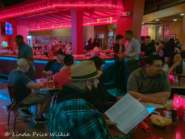 A photos with diners sitting at tables with hot pink flaming candles in front of the neon pink lighted bar.