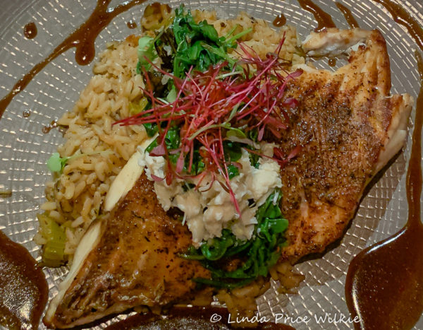 A photo of a redfish topped with blue crab and served with spiced dirty rice and wilted Winter greens.
