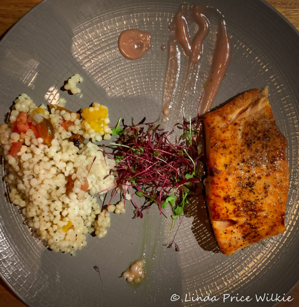 A photo of a moist, juicy honey roasted salmon sided with a pearl couscous ragout and a lemon basil salad.