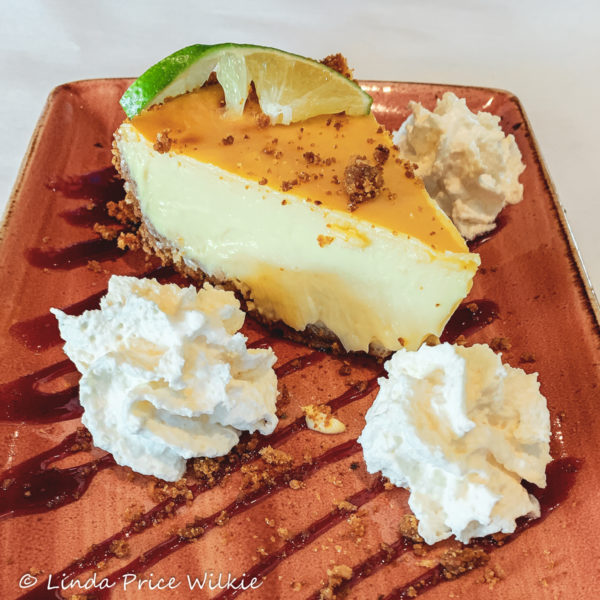 The Waterfront Restaurant's Florida Key Lime Pie made with a toasted coconut graham cracker crust, a tart and creamy lime filling, and raspberry sauce stripes topped with whipped cream clouds.